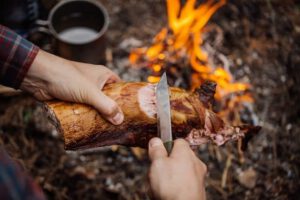 Man snijdt vlees bij kampvuur